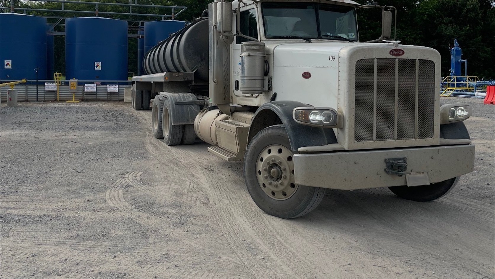 Oilfield tanker truck staged near site equipment and containment controls
